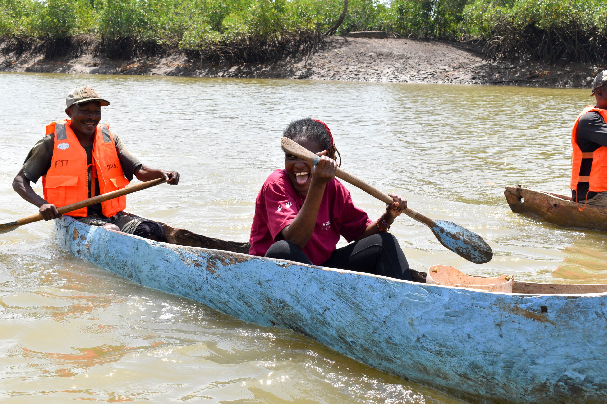A guide and visitor laughing as they paddle a canoe through the mangrove creek